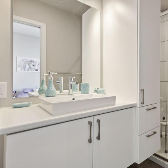 a white bathroom with a sink, mirror, and shower.