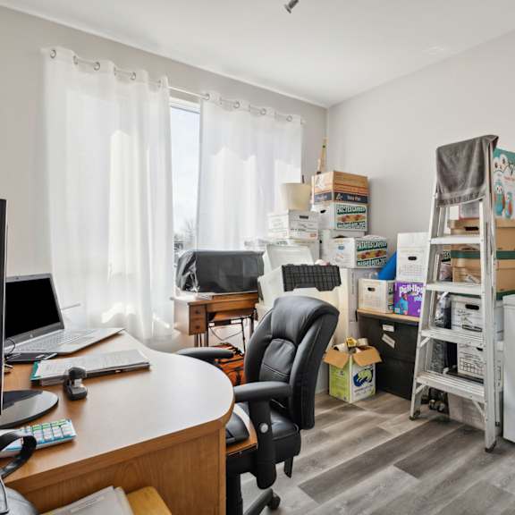 a room with a desk, chair, and a white refrigerator.