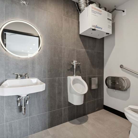a bathroom with a round mirror, a sink, a urinal, and a toilet.
