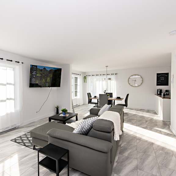 a living room with a grey couch and a television mounted on the wall.
