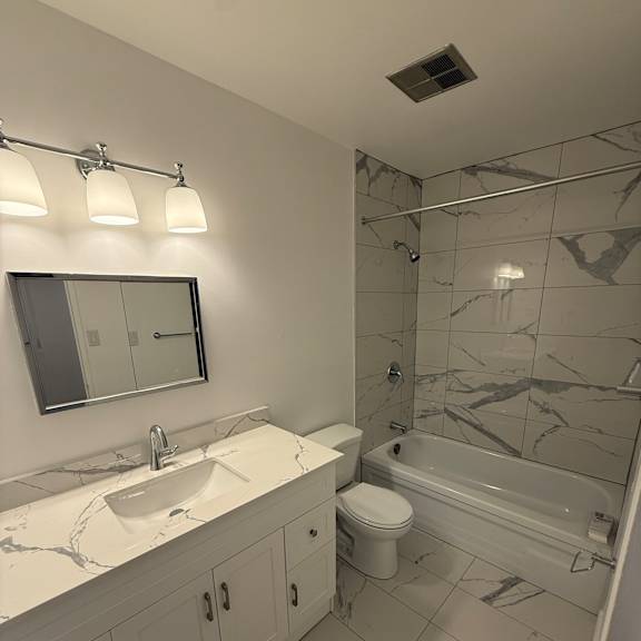 a bathroom with a marble tile shower and a white sink.