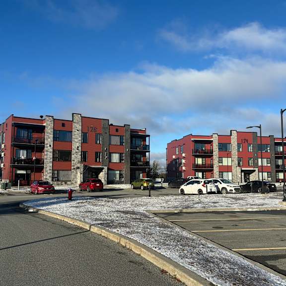 a parking lot in front of a red and grey apartment building.