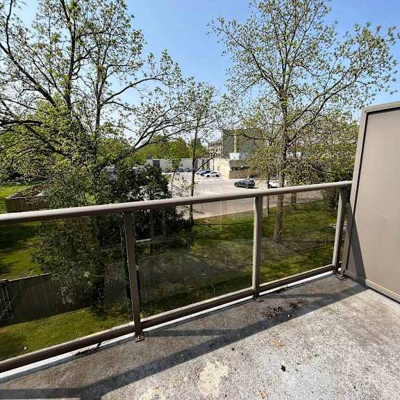 a balcony with a metal railing and a view of a parking lot and trees.
