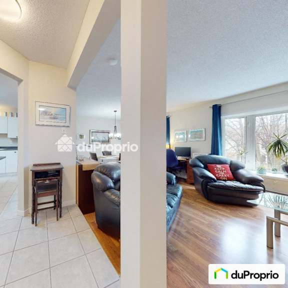 a living room with a black leather couch and a kitchen area with white cabinets.