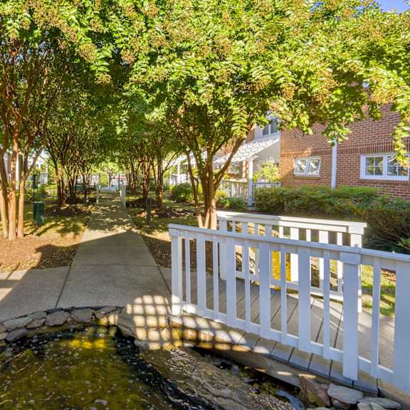 a white bridge crosses a small stream in a sunny garden.