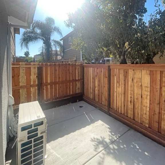 a wooden fence and a white air conditioning unit are on a patio.