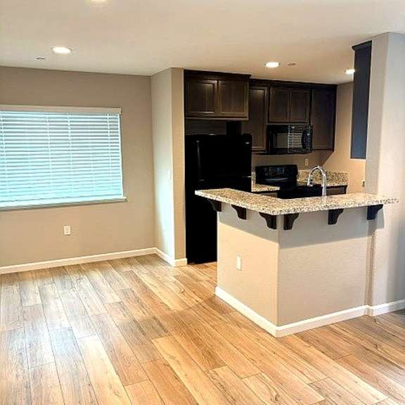 a kitchen with a black refrigerator and wooden floors.