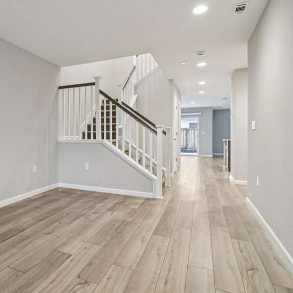 a long hallway with a staircase and wood flooring.
