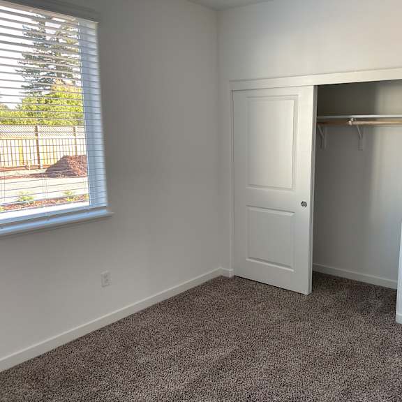 a room with a carpeted floor and a white closet with a shelf.