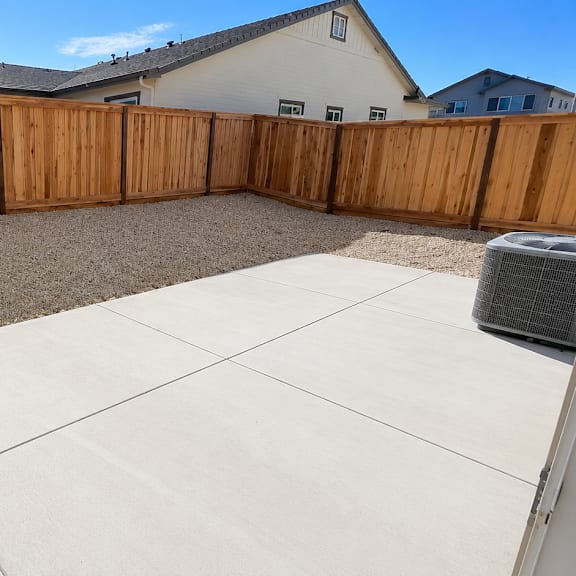 a backyard with a wooden fence and a concrete patio.
