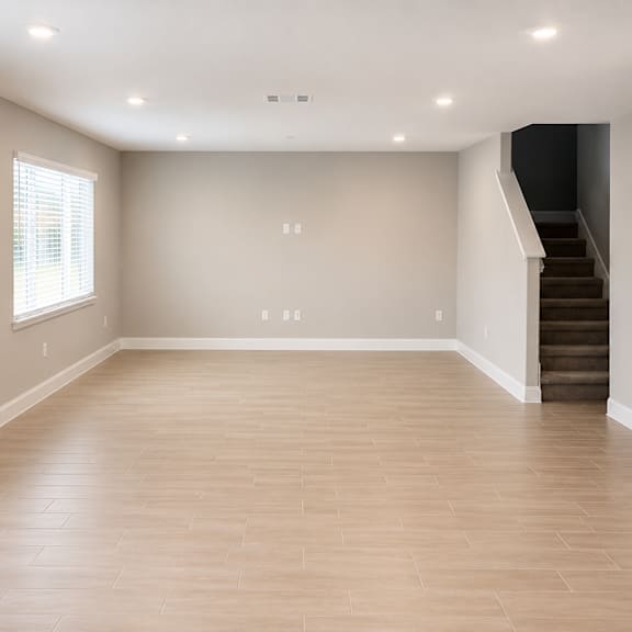 a spacious room with wooden flooring and a staircase on the right side.