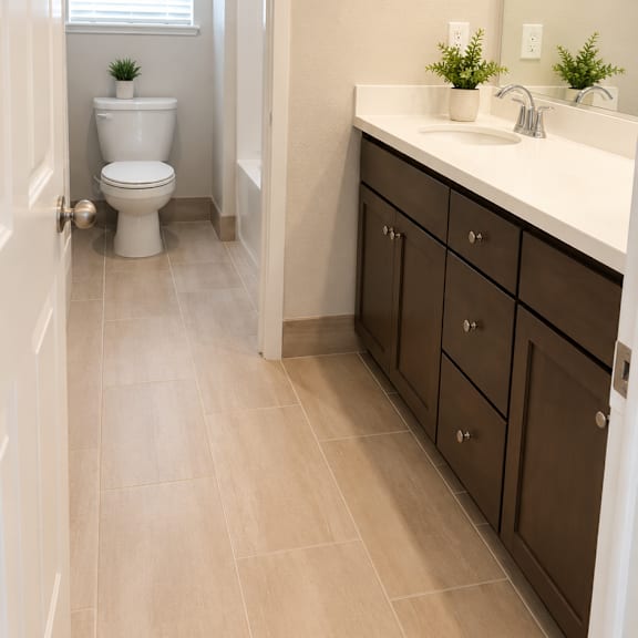 a white toilet is in a small bathroom with a sink and brown cabinets.
