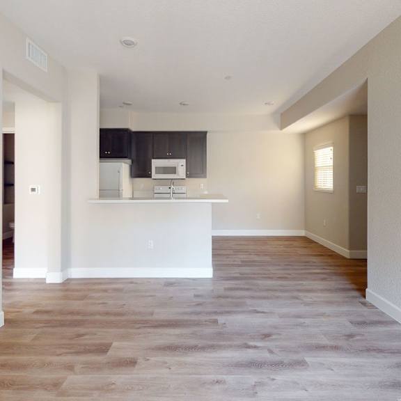 an empty living room and kitchen with white walls and wood flooring at heritage landing apartments, california, 95973