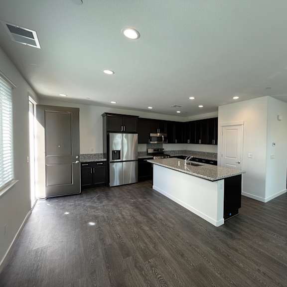 a spacious kitchen with dark wood flooring and white walls.