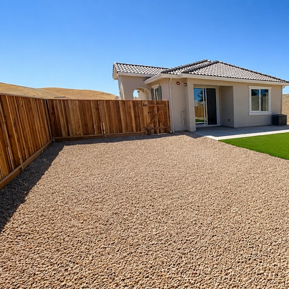 a house with a brown fence and a brown gravel driveway.