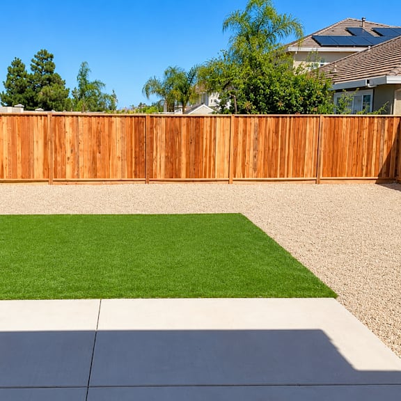 a backyard with a green lawn and a brown fence.