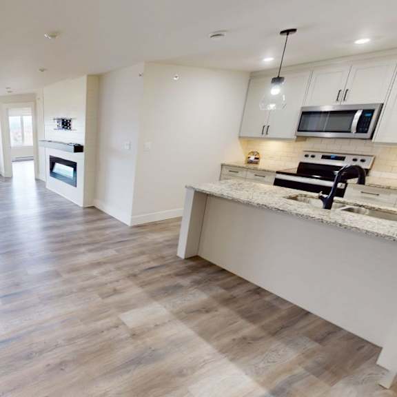 a spacious kitchen and living room with wooden flooring and white walls.