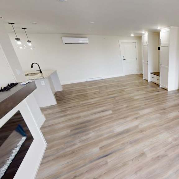 a spacious room with wooden flooring and white walls.