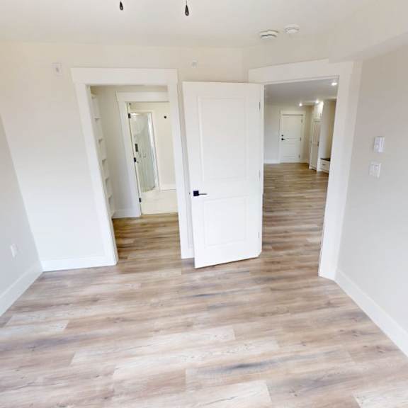 a room with white walls and wooden flooring with two open doors.