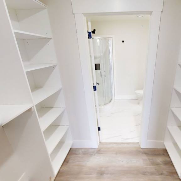 a hallway with white shelves on both sides leading to a door.