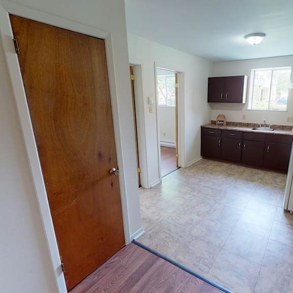 a kitchen with a refrigerator, wooden floors, and white walls.