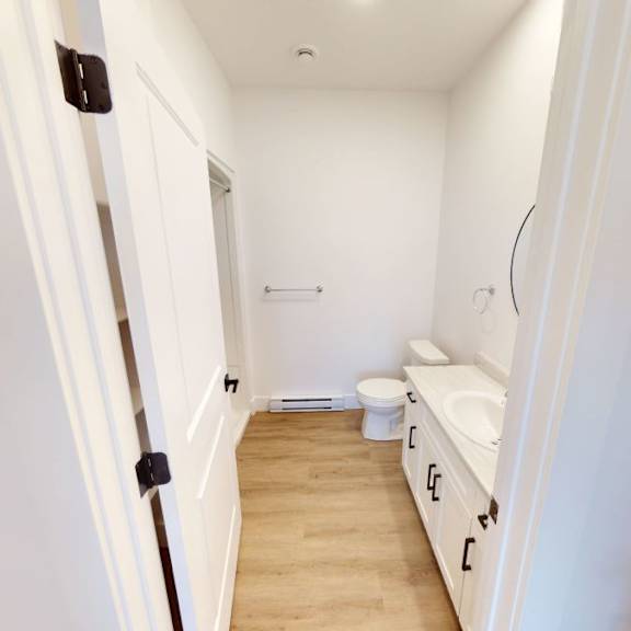 a white bathroom with a toilet, sink, and a wooden floor.