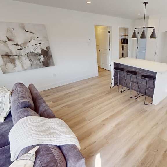 a modern living room with a grey couch and a white kitchen area.