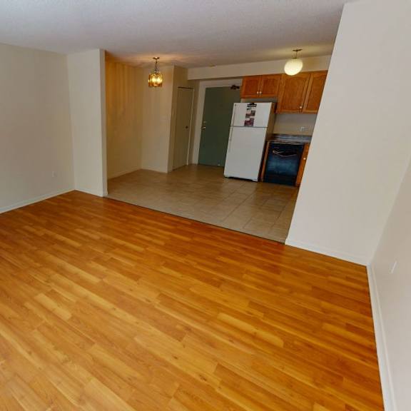 a room with wooden flooring and a kitchen in the background.