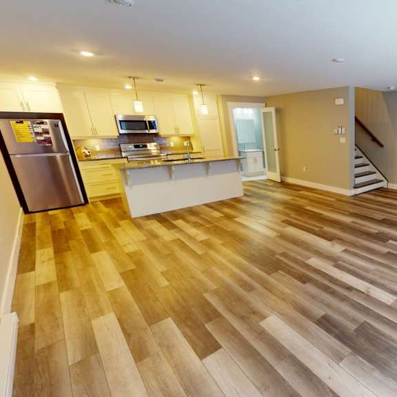 a spacious kitchen with wooden flooring and a refrigerator on the left.