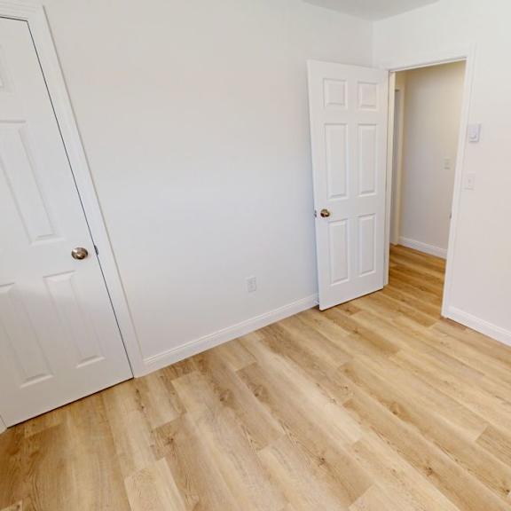 a room with white walls and wooden flooring with two doors.