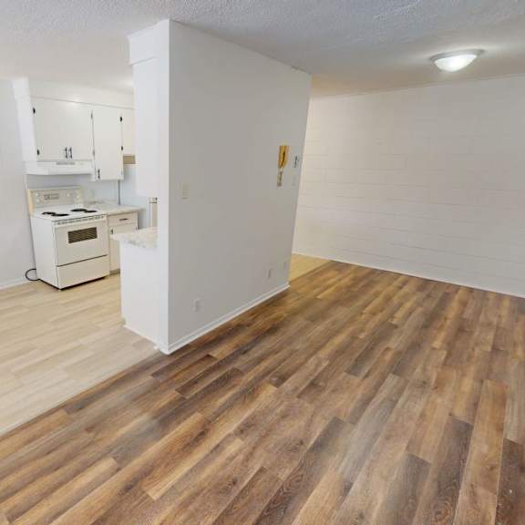 a room with wooden flooring and a kitchenette in the background.