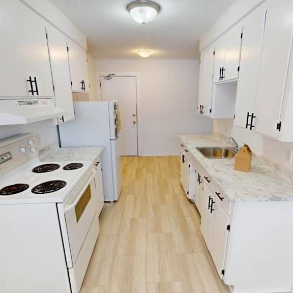 a small white kitchen with a stove, sink, and cabinets.