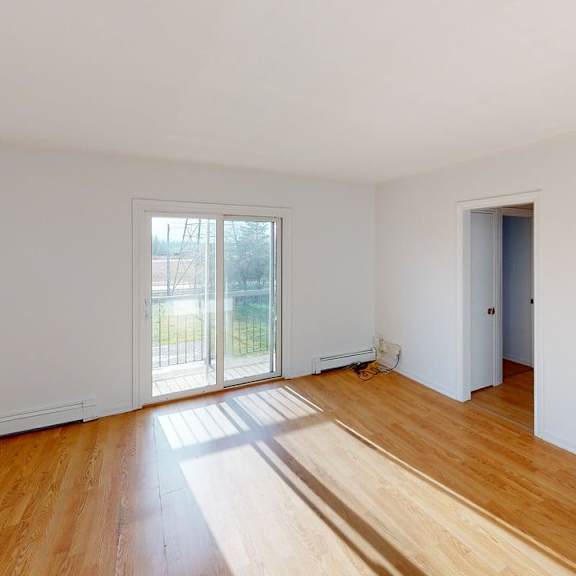 a room with wooden floors and white walls, with a door on the right and a window on the left.