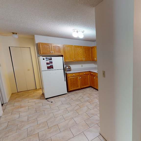 a kitchen with a refrigerator, wooden cabinets, and a tile floor.