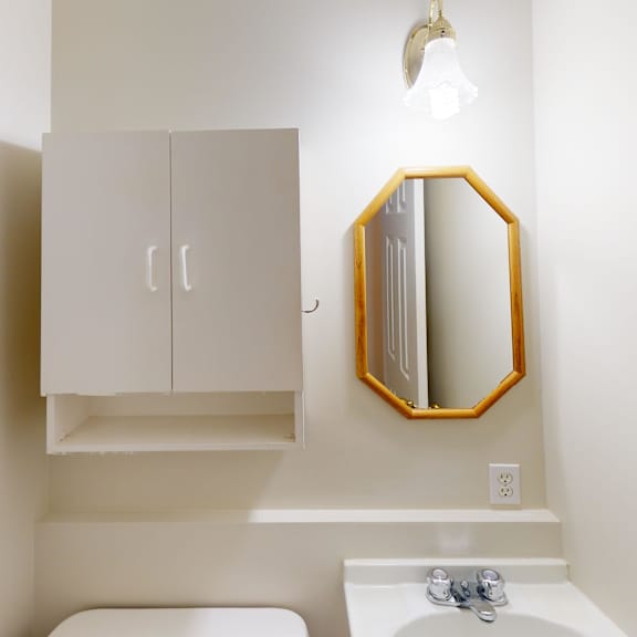 a bathroom with a white toilet, sink, and a mirror with a gold frame.