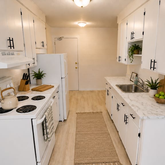 a white kitchen with a stove, sink, and cabinets.