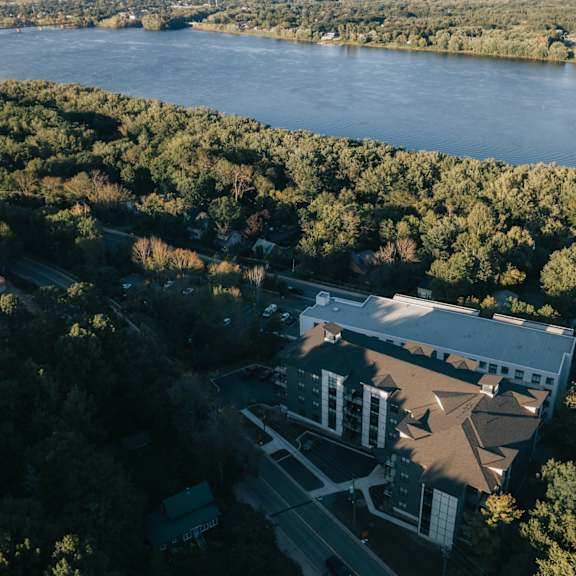 an aerial view of a building surrounded by trees with a body of water in the background.
