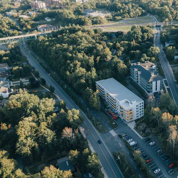 a road with cars and a white building in the middle of a forest.
