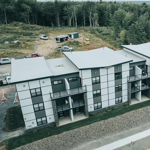 a modern building with a white and black exterior is surrounded by a wooded area.
