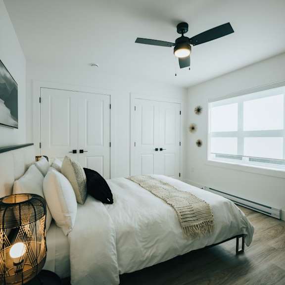 a bedroom with a bed, pillows, a lamp, and a ceiling fan.