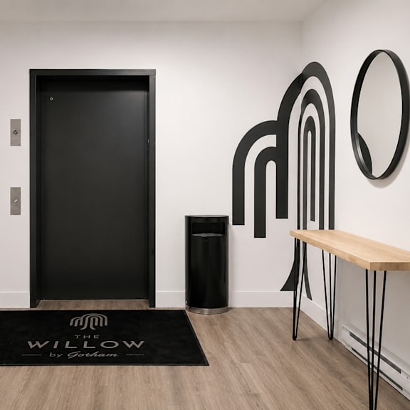 a black door is in a room with a wooden bench and a black trash can.