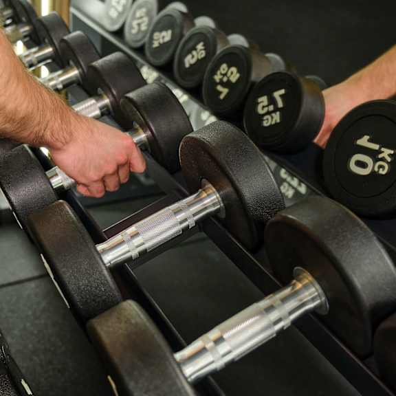 a person is selecting a dumbbell from a rack in a gym.