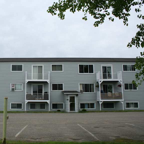 a grey apartment building with a parking lot in front.