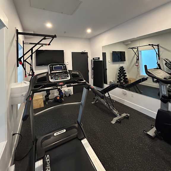 the image shows a room with a black and white interior, featuring a treadmill and a small table with a monitor on it.