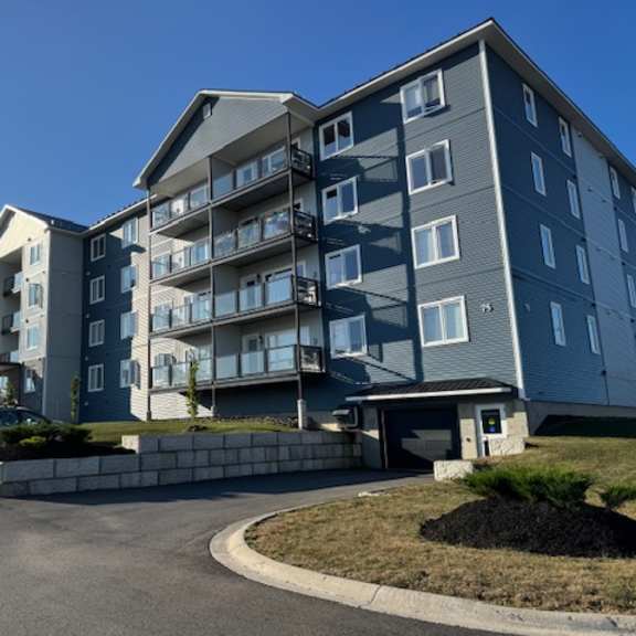 apartment complex with grey and blue buildings and cars parked in the driveway.