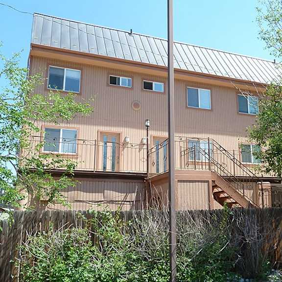 a brown house with a metal roof and a tree in front.