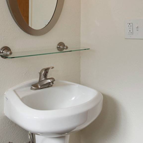 a white pedestal sink with a chrome faucet and a glass shelf above it.