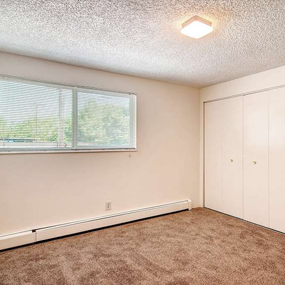 a room with a window, carpeted floor, and white cupboards.
