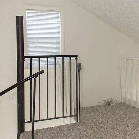 a room with a carpeted floor and a staircase with a black railing.