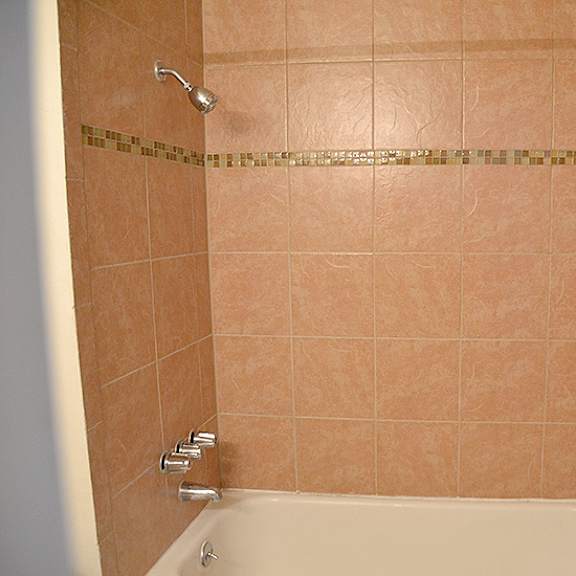 a tiled shower with a white tub and a gold tile strip.